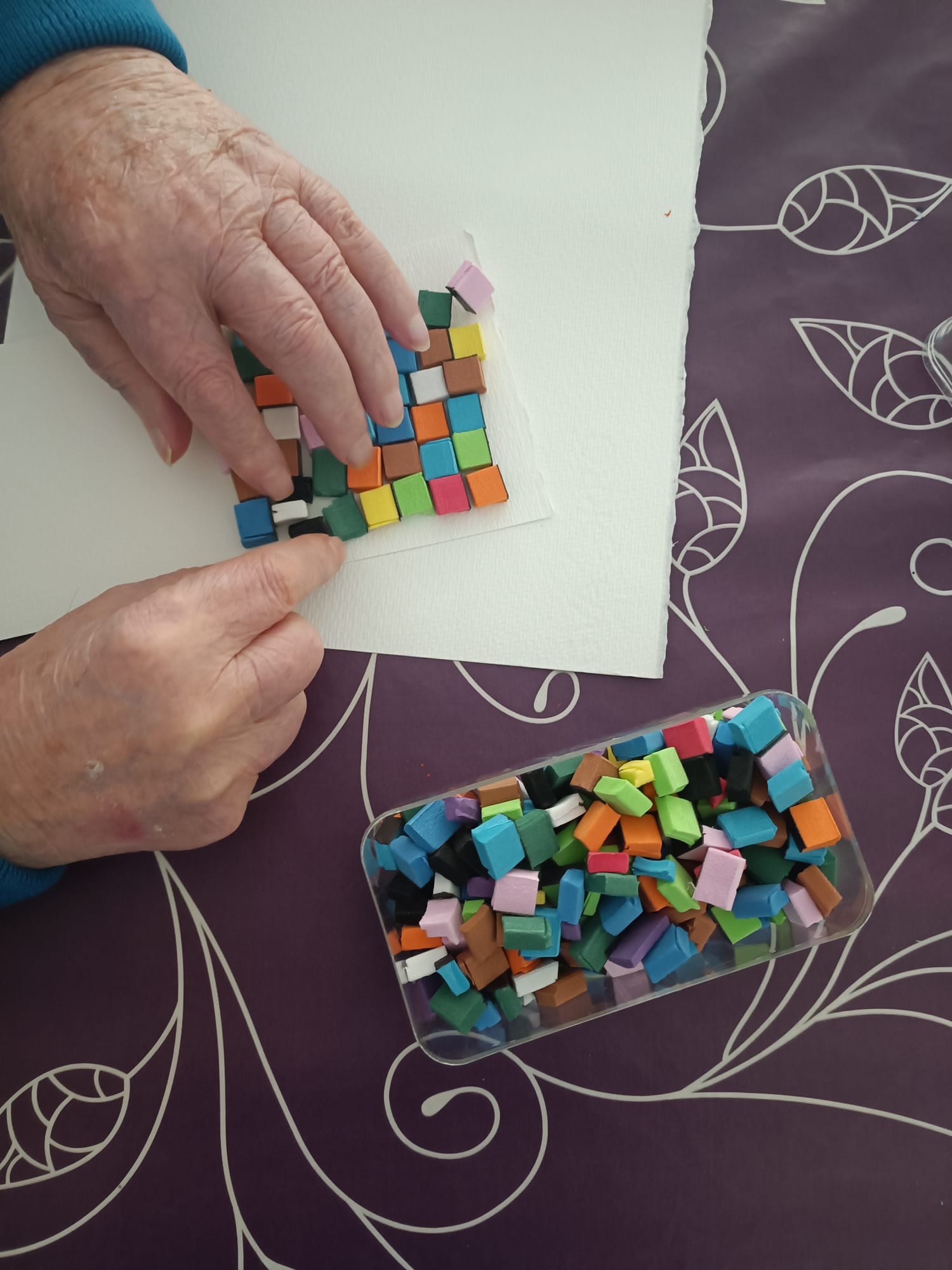 Manos de una persona mayor componiendo un mosaico de teselas de colores